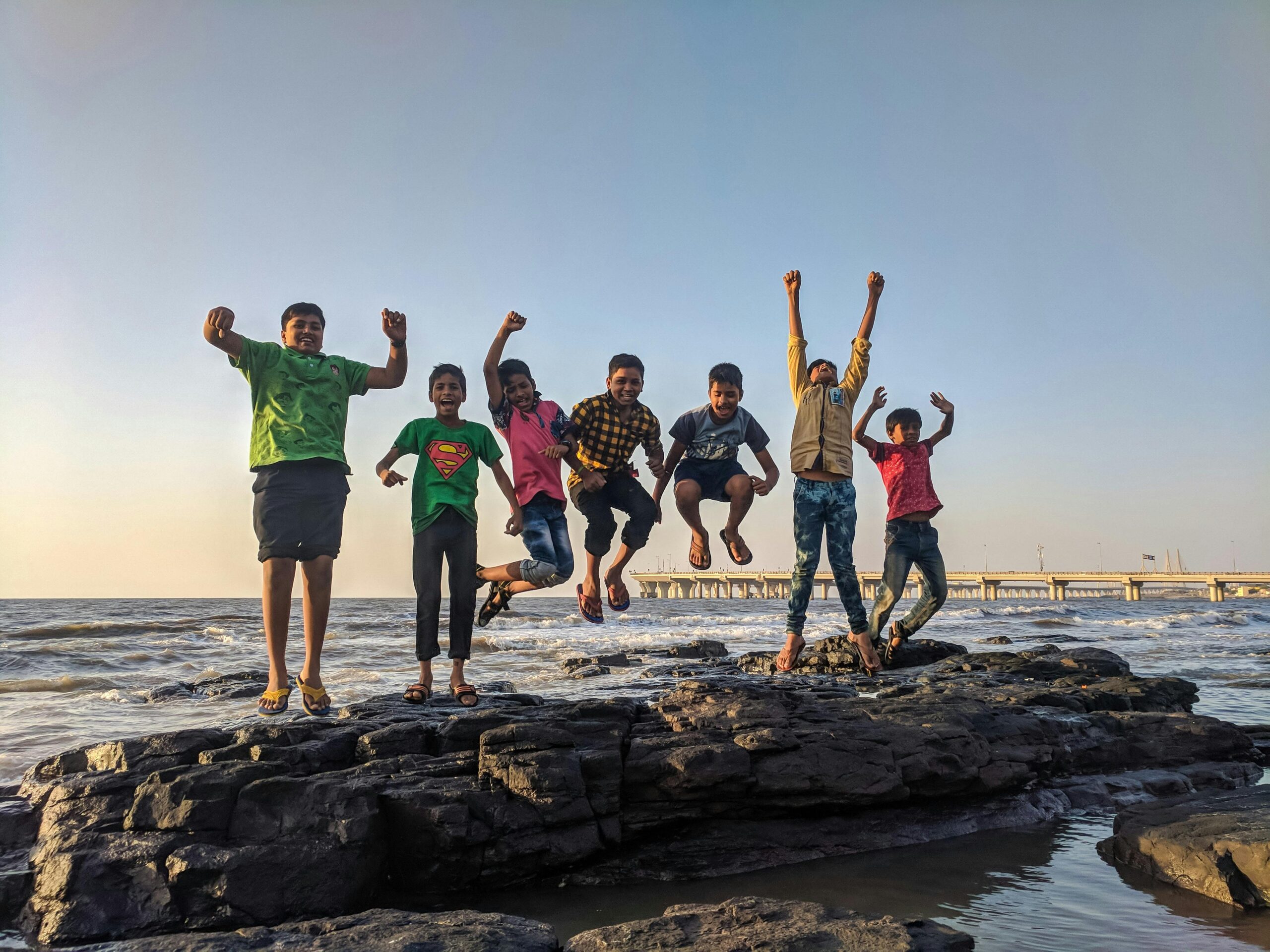 Group of kids joyfully jumping on rocks by the seaside. Fun and playful moment captured outdoors.